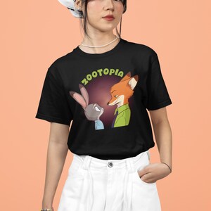May include: A black t-shirt featuring a graphic of Judy Hopps and Nick Wilde from the film Zootopia. The text "Zootopia" is written in green letters above the characters.