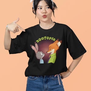 May include: A black t-shirt featuring a graphic of Judy Hopps and Nick Wilde from the film Zootopia. The text "Zootopia" is printed in green letters above the characters.