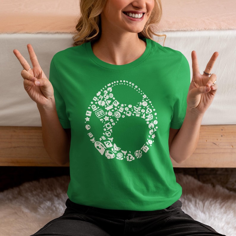 May include: Green t-shirt with a white graphic design. The design is a stylized oval shape filled with various white icons and shapes. The shirt is made of a soft material.