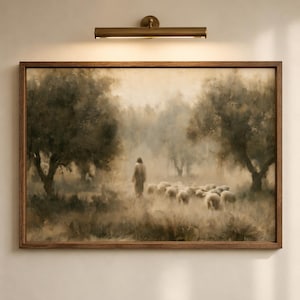 Good Shepherd Christian wall art displayed in a wood frame beneath a brass picture light, featuring Jesus walking with sheep in a soft neutral landscape.