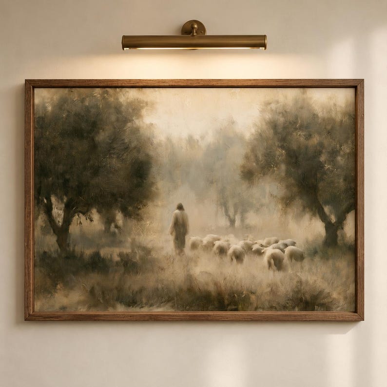 Good Shepherd Christian wall art displayed in a wood frame beneath a brass picture light, featuring Jesus walking with sheep in a soft neutral landscape.