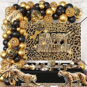 May include: A party scene with a black table, leopard print backdrop, and gold and black balloons. The backdrop reads "Happy Birthday" in gold lettering. Decorative leopard print figurines and a cake are on the table.