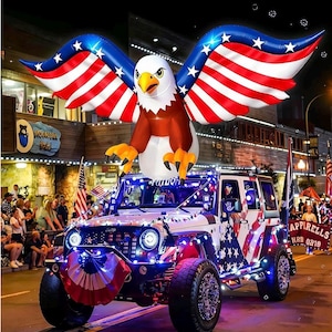 May include: A large inflatable bald eagle with wings patterned like the American flag mounted on top of a white Jeep Wrangler decorated with patriotic lights, a flag-themed grille cover, and American flag decals on the side panels.