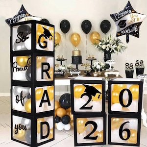 Decoración para fiesta de graduación 2026: cajas de globos negros con letras "Graduado 2026 y muy orgulloso de ti" y 20 globos.