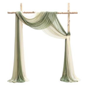 以下が含まれることがあります： 流れるような生地がかけられた素朴な木製のアーチ。生地は緑とクリーム色のグラデーションで、柔らかくエレガントな外観を作り出しています。アーチは自然な木製のポールで構成されており、結婚式やイベントに最適です。