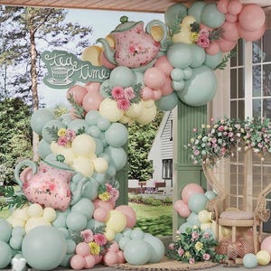 Puede incluir: Una escena caprichosa de fiesta de té con globos pastel en rosa, verde menta y amarillo, dispuestos alrededor de un arco decorativo. El arco presenta decoraciones en forma de tetera y las palabras "tea time". Una silla de mimbre y arreglos florales completan la decoración festiva.
