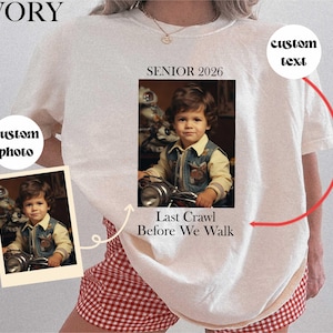 May include: Ivory-colored t-shirt with a photo of a child on a toy motorcycle. The shirt has the text "SENIOR 2026" and "Last Crawl Before We Walk". A small photo of the child is on the left side of the shirt.