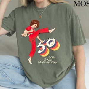 A person wearing a green t-shirt with a graphic design depicting a woman in a red outfit and the number "50" on it.