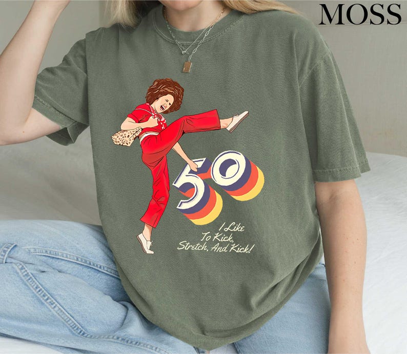 A person wearing a green t-shirt with a graphic design depicting a woman in a red outfit and the number "50" on it.