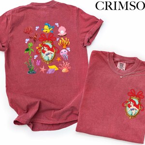 a red t-shirt with a mermaid design and various marine-themed illustrations, including a mermaid, fish, and coral.