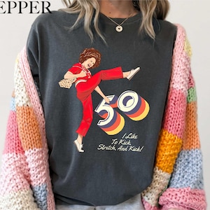 A person wearing a black t-shirt with a graphic design depicting a woman in a red outfit and the number "50" on it.