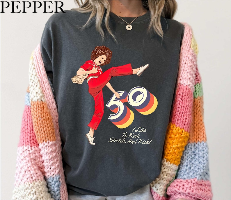 A person wearing a black t-shirt with a graphic design depicting a woman in a red outfit and the number "50" on it.