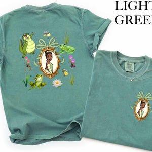 a green t-shirt with a design of a princess surrounded by various cartoon characters and elements, such as a frog, flowers, and a bow.
