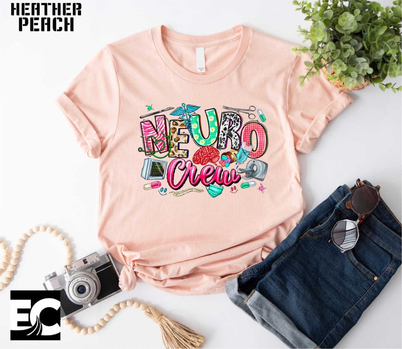 a pink t-shirt with a colorful graphic design, a pair of blue jeans, a camera, and some accessories such as a plant and sunglasses.