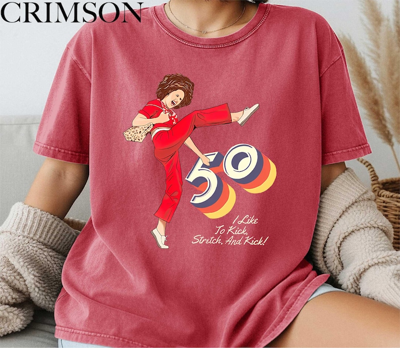 A red t-shirt with a graphic design depicting a woman in a red outfit with the number "50" on it. The text below the graphic says "I Like To Kick Stretch And Rick!"