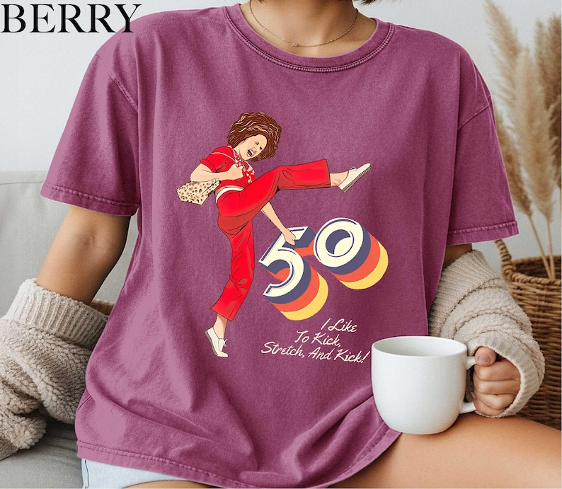 A person wearing a purple t-shirt with a graphic design of a woman in red pants and a white top, along with the text "I like to kick, stretch, and kick!"