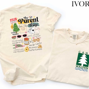 May include: Ivory-colored t-shirts. One shirt features a graphic with the text "The Parent Trap" and various illustrations. The other shirt has a green and white tree graphic with the text "Camp Walden".