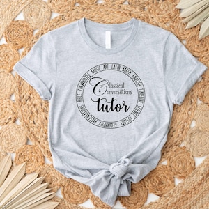 May include: Gray t-shirt with a black circle graphic that says "Classical Conversations Tutor" and lists subjects like Bible, Tin Whistle, Music, Art, Latin, Math, English, Timeline, Science, History, and Geography.