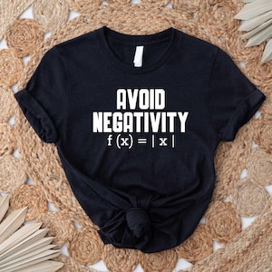 May include: Black t-shirt with the words "AVOID NEGATIVITY" in bold white letters, followed by the mathematical expression f(x) = |x|. The shirt is knotted at the waist and rests on a woven beige surface.