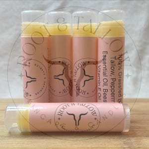 May include: Lip balm tubes with a light pink label and clear cap. The label includes the text "Root & Tallow Skincare & Candles". The lip balm is yellow. The ingredients include tallow, peppermint oil, and vitamin E oil.