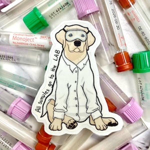 Può includere: Un adesivo bianco con un'illustrazione di un labrador retriever giallo in stile cartone animato che indossa un camice da laboratorio bianco e occhiali protettivi. Il cane è seduto con le zampe incrociate. Il testo "All samples go to the LAB" è scritto in nero sull'adesivo. L'adesivo è sopra un mucchio di provette di plastica trasparente con tappi rossi, verdi e viola.