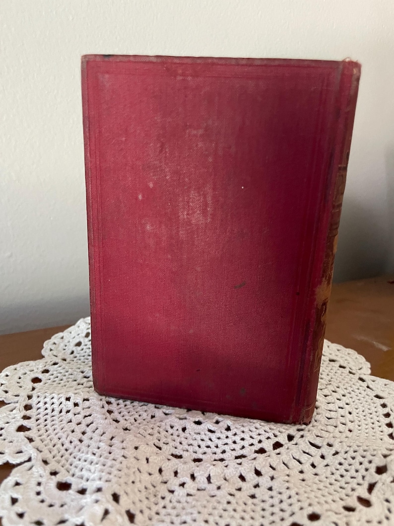 May include: A rectangular hardcover book with a solid deep red fabric cover. The front cover features a subtle embossed border frame design. The spine of the book shows signs of wear with visible fraying along the edges and corners of the binding.