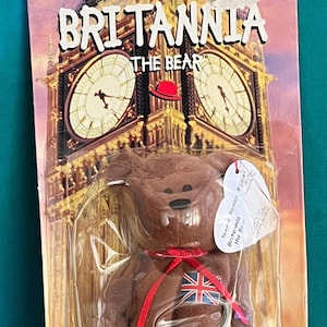 May include: A brown Britannia the Bear Beanie Baby toy in its original packaging. The packaging features an image of Big Ben and the text "Britannia the Bear". The bear has a red ribbon and a Union Jack on its chest.
