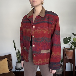 Puede incluir: Chaqueta roja estampada con cuello y detalles de bolsillo de ante marrón. La chaqueta tiene botones dorados y un diseño geométrico en tonos rojos, verdes y dorados. La chaqueta está abotonada.