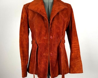 May include: A burnt orange suede jacket with a notched collar and button closure. The jacket features long sleeves, a fitted waist with belt loops, and decorative stitching. The jacket is displayed on a mannequin against a white background.