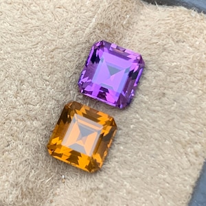 May include: Two square-cut gemstones. One is a vibrant purple, the other a rich orange. Both have a faceted design, catching the light. The gems are displayed on a textured, beige surface, showcasing their brilliance.