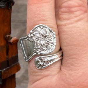 May include: A silver spoon ring with a floral design. The ring is made from a vintage spoon and features a delicate flower pattern.