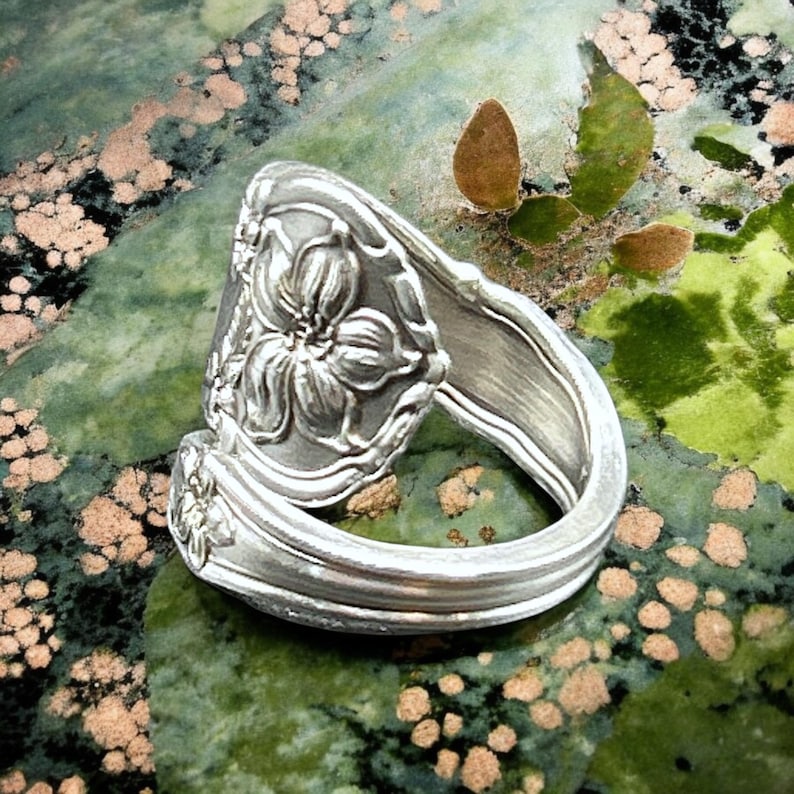 May include: A silver spoon ring with a floral design. The ring is made from a repurposed spoon and features a detailed flower design.