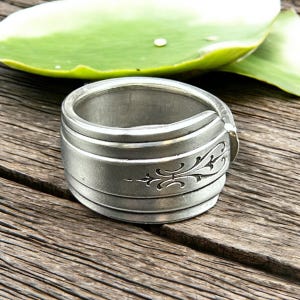 May include: A silver ring made from a repurposed spoon. The ring is wide and has a decorative design on the band.