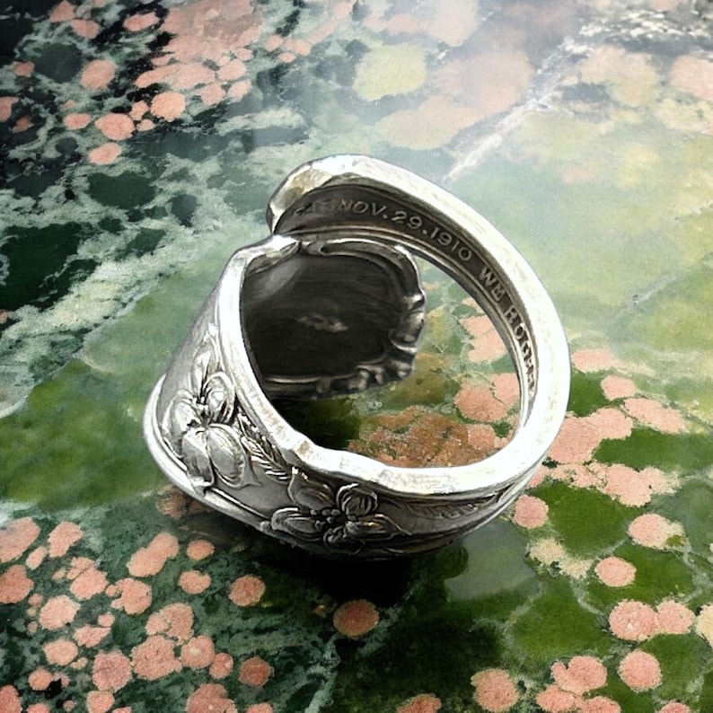 May include: A silver spoon ring with a floral design and the inscription "NOV. 29. 1910 WE HOME".