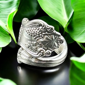 May include: A silver spoon ring with a grapevine design. The ring is made from a vintage spoon and is a unique piece of jewelry.