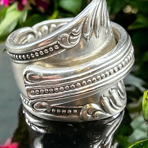 Puede incluir: Un anillo de plata hecho de una cuchara reutilizada. El anillo está retorcido y tiene un diseño decorativo en la parte superior.