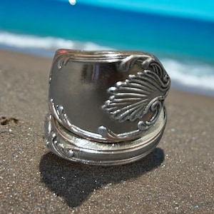 May include: A silver spoon ring with a decorative design on the band. The ring is made from a repurposed spoon and has a unique, handcrafted look.