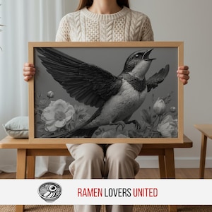 May include: A framed black and white print of a bird with outstretched wings and an open beak, set against a floral background. The artwork is held by a person. The frame is made of light-colored wood.