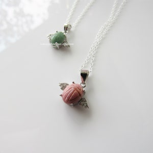 May include: Two silver necklaces with winged scarab beetle pendants. One pendant is green and the other is pink.