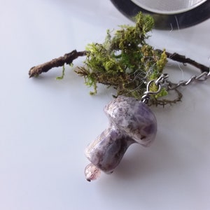 May include: A purple and white mushroom-shaped tea infuser with a silver chain attached to a small piece of moss.