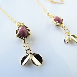 以下が含まれることがあります： ピンクの宝石のアクセントと金の葉のチャームが付いた、金のイヤリングのペアです。