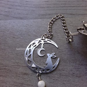 May include: Silver charm featuring a crescent moon with a rabbit silhouette, a small moon charm, and a white gemstone hanging from the bottom.