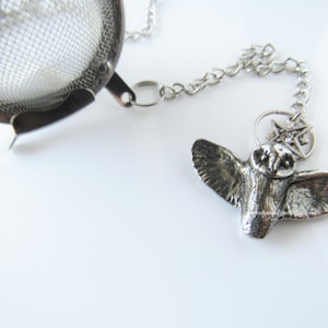 May include: Silver tea infuser with a chain and a small owl charm with a star on top.