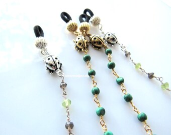May include: Three pairs of glasses retainers with ladybug charms and green and brown beads. The retainers are made of black elastic and gold chain.