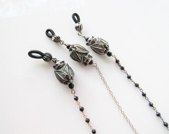 May include: Three black and silver eyeglass chains with bat charms. Each chain has black beads and a different style of clasp.