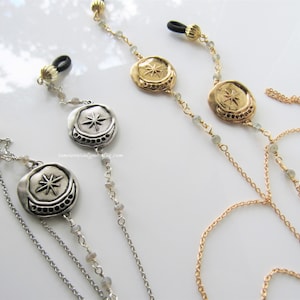 May include: Two pairs of eyeglass chains with silver and gold tone metal charms. Each charm features a star and crescent moon design. The chains are made with silver and gold tone metal, and clear beads.