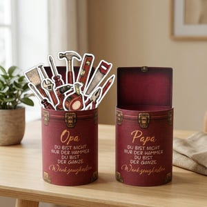 May include: Two burgundy-colored cylindrical containers with hinged lids, resembling small trunks. One is open and filled with tool cutouts. Text on the containers reads "Opa" and "Papa" with German text. Decorative metal clasps and corner accents.