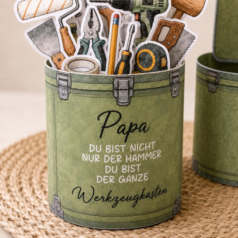 May include: A green toolbox-shaped container with the word "Papa" in cursive script. The container is filled with paper cutouts of tools. The text "DU BIST NICHT NUR DER HAMMER DU BIST DER GANZE Werkzeugkasten" is also visible.