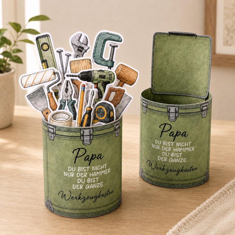 May include: Two olive green decorative tool boxes with the word "Papa" and German text. One box is open, and both are filled with tool-themed stickers, including a level, wrench, and drill. The boxes are on a wooden surface.