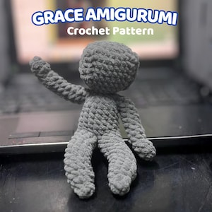 Puede incluir: Muñeca amigurumi gris tejida a ganchillo con un brazo y piernas extendidas. La muñeca está hecha de hilo texturizado y tiene una cabeza redonda. El texto encima de la muñeca dice "GRACE AMIGURUMI Crochet Pattern".